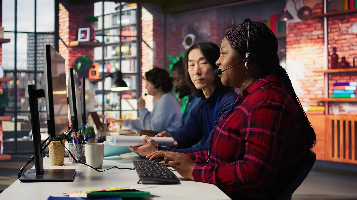 Primer plano de un trabajador con experiencia hablando con un cliente mediante el micrófono de unos auriculares.